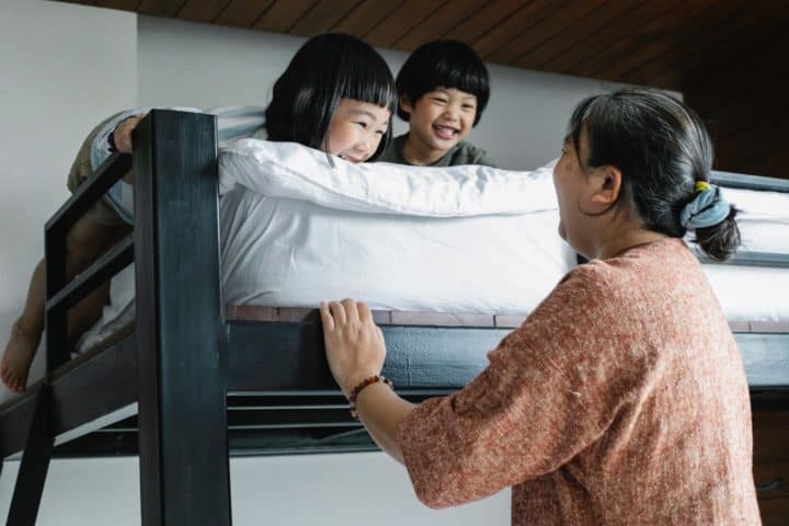 Two kids on bunk bed with grandma standing next to it